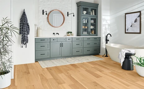 Light hardwood flooring in bathroom with dark grey cabinets and white stone countertops