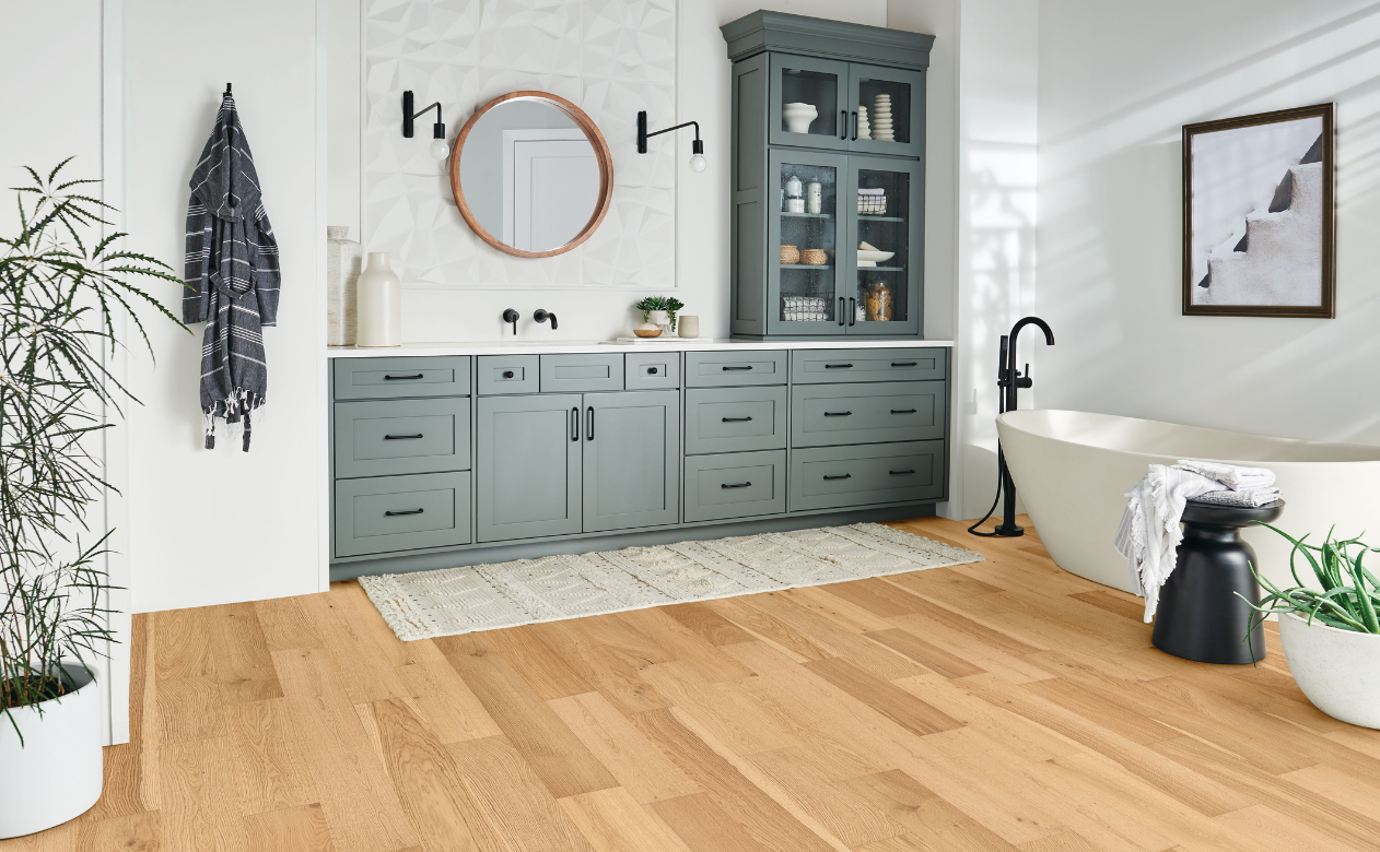 Light hardwood flooring in bathroom with dark grey cabinets and white stone countertops